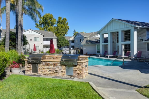 a backyard with a pool and a barbecue grill in front of a house at The Legacy Apartments, Antelope, CA