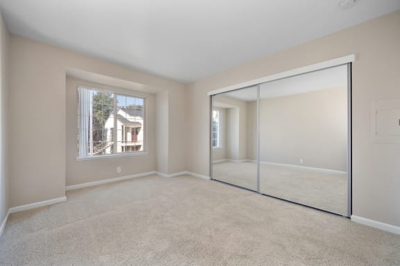 an empty living room with a large window and a mirrored closet