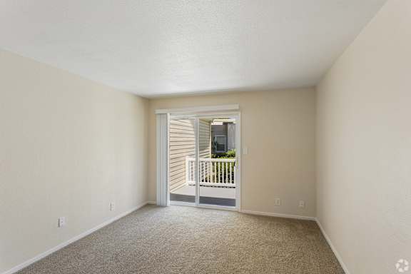 A room with a carpeted floor and a doorway leading to a balcony.