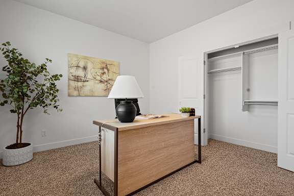 A room with a wooden desk, a potted plant, and a painting on the wall.