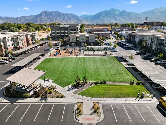 A large grassy area in the middle of a parking lot with buildings and mountains in the background.