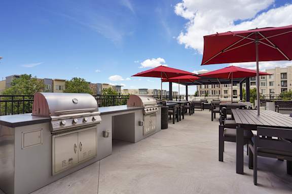 A patio with tables and grills under red umbrellas.