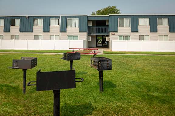 A black sign is in the foreground of a grassy area in front of a building.