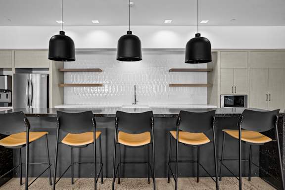 A modern kitchen with black chairs and a white backsplash.
