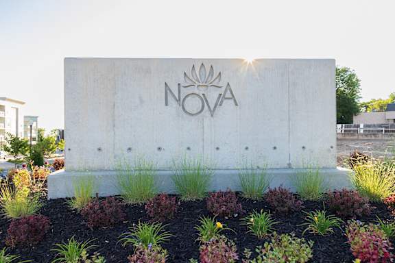 A concrete sign with the word NOVA on it is surrounded by plants.