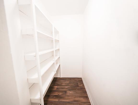 A long white shelving unit with multiple shelves is in a room with white walls and wooden flooring.