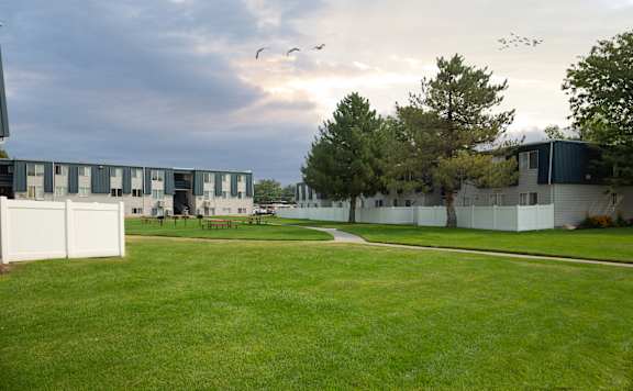 A grassy field with a building in the background and birds flying in the sky.