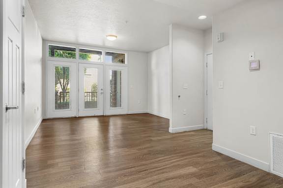 A room with white walls and wooden flooring with a door on the left.