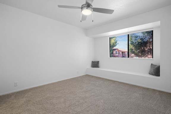 A room with a ceiling fan and a window with a view of a house.