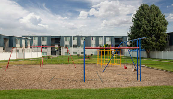 A playground with a swing set and a building in the background.