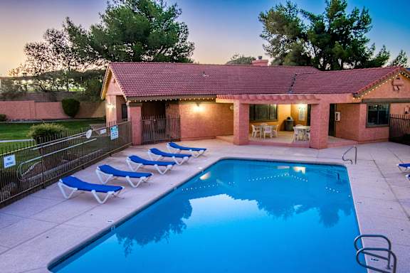 A pool with blue loungers and a house with a red roof.
