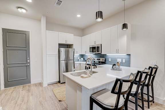 A kitchen with white cabinets and a white island with three chairs.