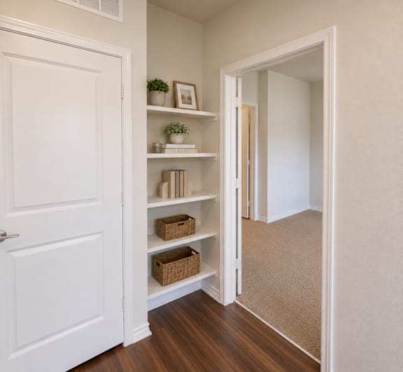 A white door is open to a hallway with a shelf and plants.