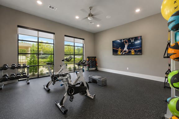 A spacious gym with a variety of exercise equipment and a basketball court visible through the windows.