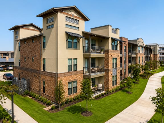 Modern apartment homes with landscaped walkways and private balconies at One Preston Station in Celina, Texas.