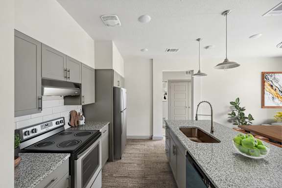 Modern apartment kitchen with a gooseneck faucet, quartz countertops, stainless steel appliances, and a large center island.