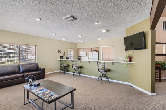 Clubhouse with a brown leather couch, a coffee table, and a flat-screen TV mounted on the wall at Horizon East Apartments in Aurora, CO