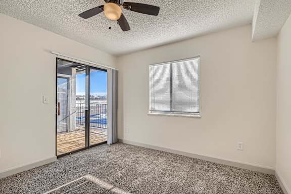 A room with a ceiling fan and a sliding glass door leading to a balcony.