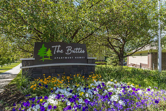A sign for The Butter Apartment Home is surrounded by flowers  at The Buttes Apartments Loveland, CO.
