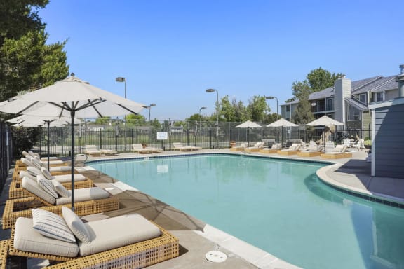 a pool with lounge chairs and umbrellas in front of a building at Horizon East Apartments in Aurora, CO