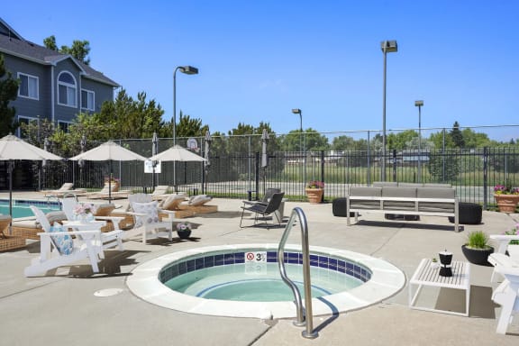 a hot tub sits in the middle of a patio with lounge chairs and umbrellas at Horizon East Apartments in Aurora, CO