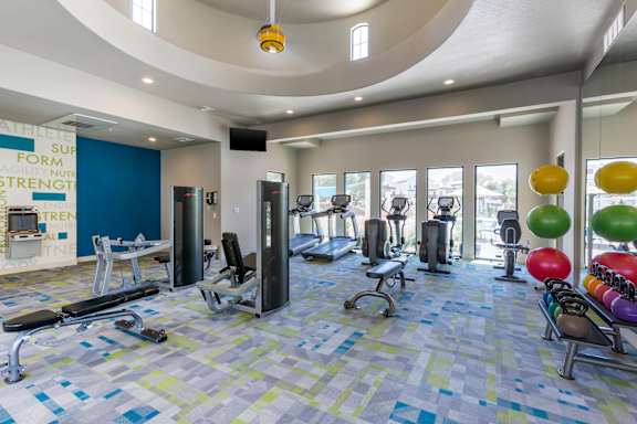 a gym with cardio equipment and weights in a large room with windows at Trevi Apartment Homes, Chandler, AZ, 85224