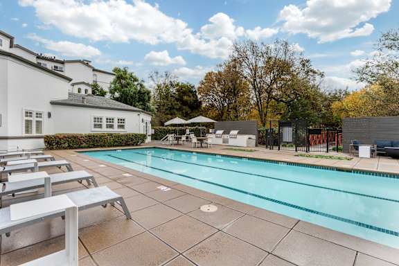 A swimming pool surrounded by lounge chairs and a white building.