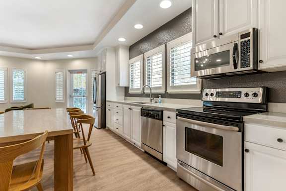 A modern kitchen with stainless steel appliances and wooden chairs.