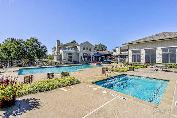 A large outdoor swimming pool surrounded by a concrete patio and a building in the background.