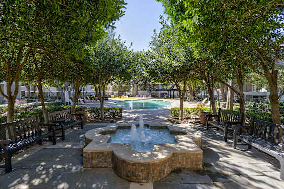 A fountain in the middle of a park surrounded by benches and trees.