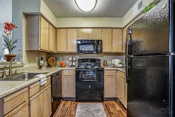 A kitchen with wooden cabinets and a black refrigerator at Trinity Square Apartments, Dallas Texas