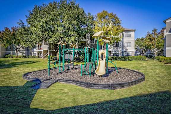 A playground with a green swing set and a yellow slide at Saxony at Chase Oaks Apartments, Plano