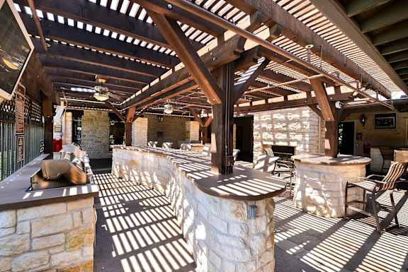 A large open patio with a stone fireplace and wooden beams at Cypress Lake at Stonebriar Apartments, Texas