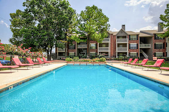 A large swimming pool in front of a building with red lounge chairs on the side at Greenbriar Apartments, Tulsa, OK 74136
