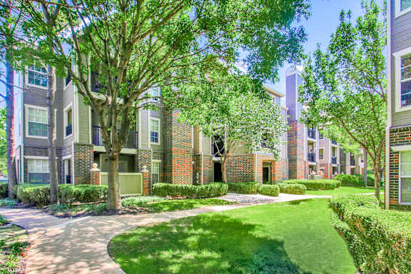 A tree-lined walkway leads to a brick building at Riverside Park Apartments, Tulsa