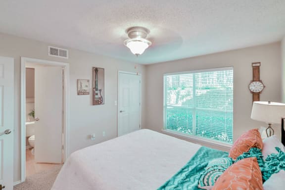 A bedroom with a bed, a window with blinds, a lamp, and a wall clock.
