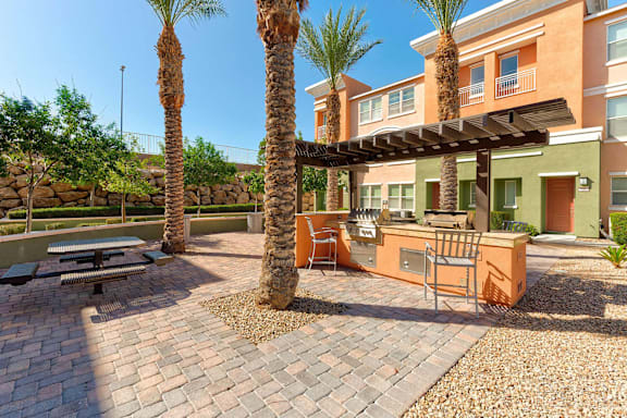 A patio with a table and chairs under a pergola with palm trees in the background.