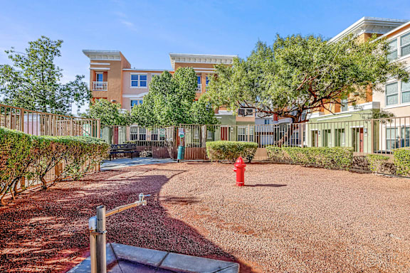 A playground with a red fire hydrant in the middle of a gravel area.