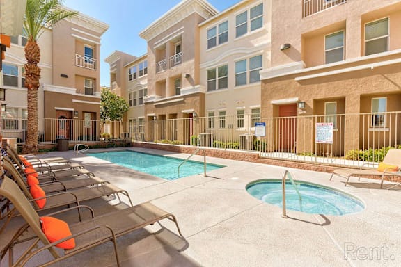A pool area with chairs and a fence in front of apartment buildings.