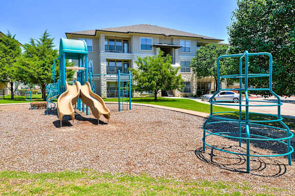 A playground with a slide and a climbing frame in front of a building at Cypress Lake at Stonebriar Apartments, Frisco