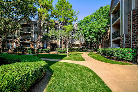 A pathway leads through a grassy area between two apartment buildings at Riverside Park Apartments, Tulsa, OK 74136