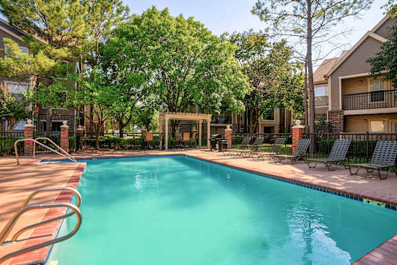 A swimming pool surrounded by trees and chairs at Riverside Park Apartments, Tulsa, OK
