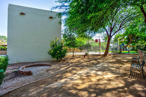 A white wall with three holes in it is surrounded by trees and a bench.
