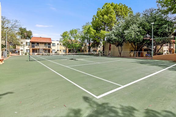 A tennis court surrounded by trees and buildings.