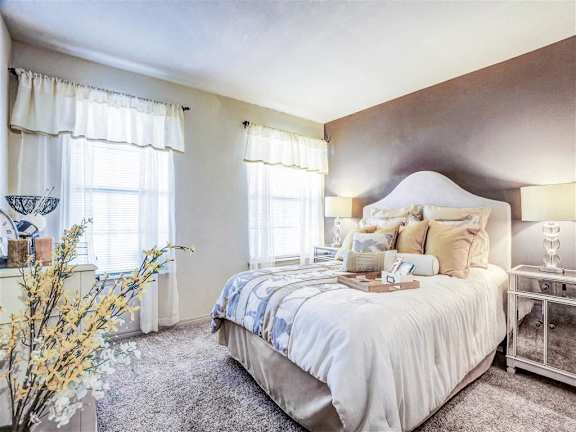 A bedroom with a large bed and a vase of flowers on the side table at Riverside Park Apartments, Oklahoma
