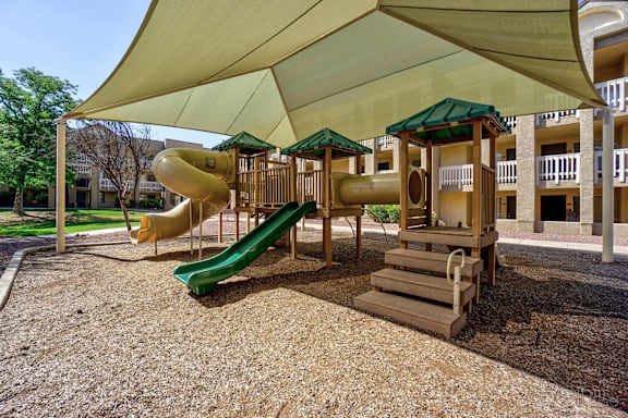 A playground with a green slide and a yellow slide under a canopy.