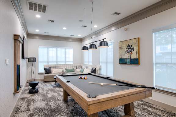 A pool table is in the middle of a room with a couch and a TV.