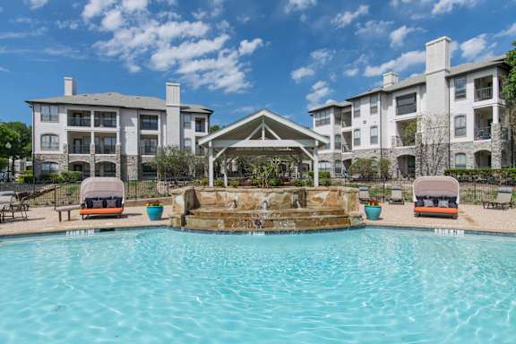 A swimming pool in front of a building with a gazebo.