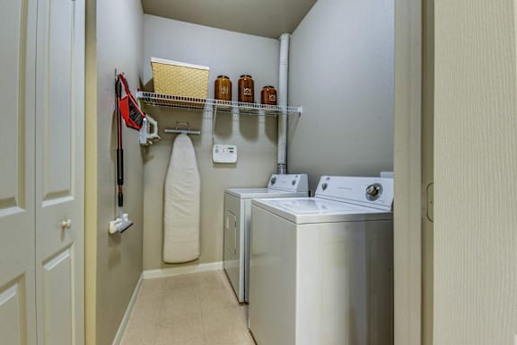 A laundry room with a washer and dryer, a towel hanging on a rack, and a shelf with three bottles on it.