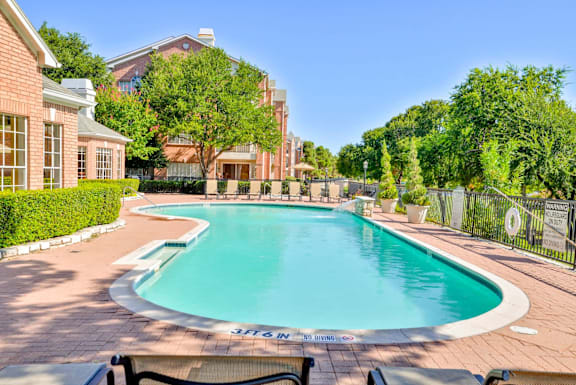 A large outdoor swimming pool surrounded by a brick patio and trees.